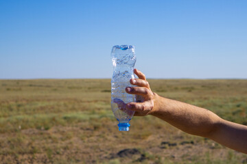 a hand holds an empty bottle in the desert. thirst, desert, not water.