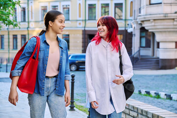 Two walking talking laughing teenage girls walking down the city street