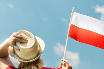 A young woman in a summer hat holds the Polish flag above her head against the sky, Concept for the celebration of national holidays