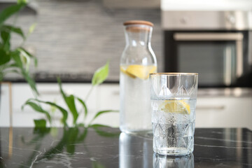 Glass with homemade lemonade in the kitchen. Summer refreshing lemonade drink. Water with lemon. 