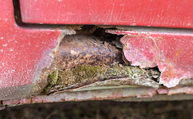 Rusty driver's door sills. Corrosion of the body of a red old car after winter. Influence of...