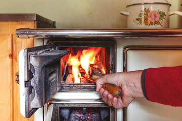 anschüren eines Feuers in einem alten Holzofen in der Küche einer Almhütte