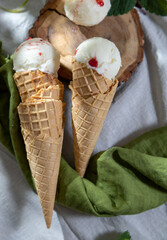 Ice cream with fresh strawberries and jam in waffle cone on plate, on rustic wooden background with a green napkin.