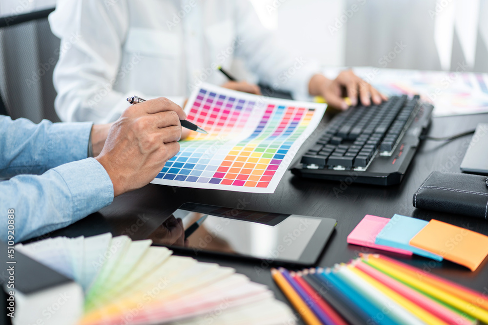 Poster Team graphic designer working on document of color chart to brainstorming about new project and using laptop