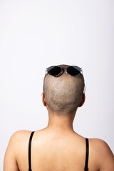 Woman standing back to camera with shaved head and sunglasses on it in white studio background with...