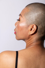 Abstract portrait. Woman standing back to camera with shaved head in white studio background with...