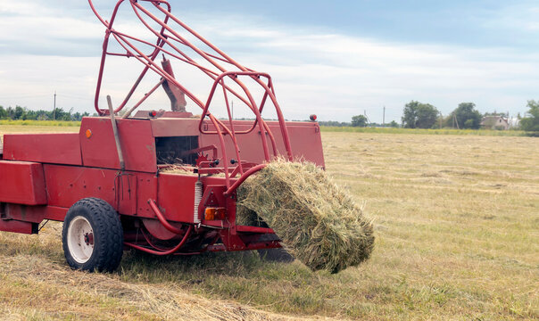 Close-up of hay baling with a tractor using a baler on a cloudy summer day, a large bale comes out of the baler.
