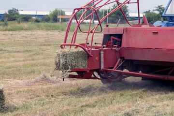 Fototapeta premium Rear side of hay baler with bale coming out and hay mowed into swath