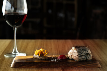 wooden board with steak, red sauce, fried sweet potato slices and glass of red wine