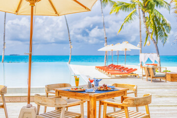 Luxury resort hotel poolside, outdoor restaurant on beach, ocean and sky, tropical island cafe, tables, food. Summer vacation or holiday, family travel. Palm trees, infinity pool, cocktails, relax