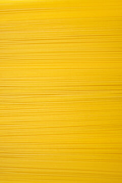 Background of long dry spaghetti arranged horizontally on a vertical photo. Traditional Italian wheat dish. Free space for text and advertising. Long narrow spaghetti ready to cook