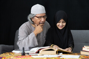 muslim father teaching his daughter about practicing reading textbook on black background