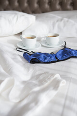 Fototapeta na wymiar two cups of coffee and a beautiful bra on a white bed, close-up