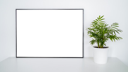 White poster on table with black frame and plant mockup for you design.