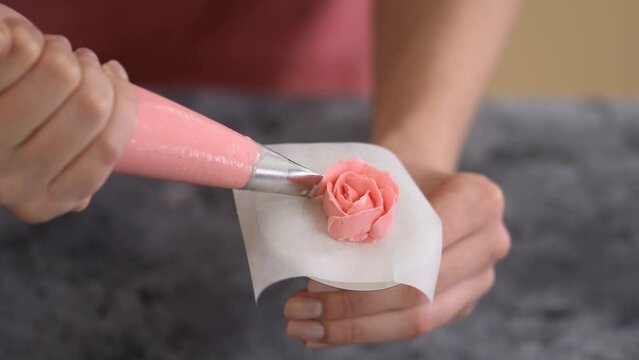 Making pink buttercream frosting roses at home. The confectioner makes flowers from cream.