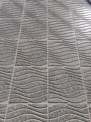 Piso de losas de concreto terrestre en la acera urbana con ondas en relieve color gris y lìneas geomètricas en olas, forma un original diseño abstracto para fondos