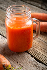 cup of fresh carrot juice with carrots around old style wooden background