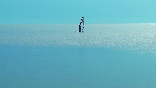 silhouette windsurfer sailing on windsurf board on sea at a beautiful sunset sky on background. Healthy active lfestyle, hobby, summer fun adventure.