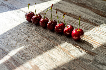 Cherry berries in water drops lined up in a row on a light wooden surface