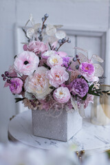 Light gray concrete planter with flowers. Gently pink anemones, pink roses and cream peonies with eucalyptus. Composition on a marble table. Floristics preserved flowers.