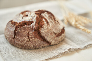 Freshly baked rye bread on a yeast-free starter and on a mixture of whole grain, rye and wheat flour. It lies on a napkin, next to a dried flower with grains. Selective focus. High quality photo