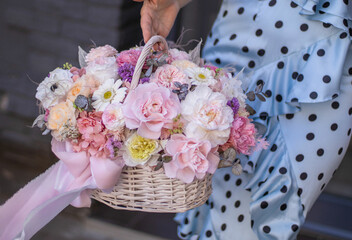 Beautiful bouquet of flowers in basket, woman hands. Wicker basket with preserved flowers. Floristry concept. Spring colors.