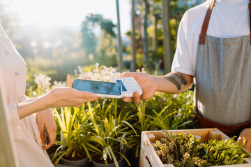 Close up of mobile payment in a garden florist shop. Woman paying with mobile