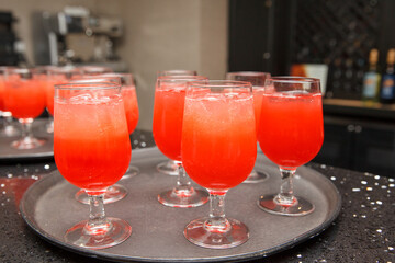 Refreshing red and orange drinks on a tray in wine glasses.
