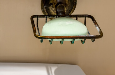 Lime-colored soap with light foam close-up in brass soap dish above wash basin in bathroom
