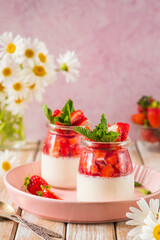 Dessert, creamy panna cotta with fresh strawberries in glass jars on a light wooden background. Dessert recipes without baking.