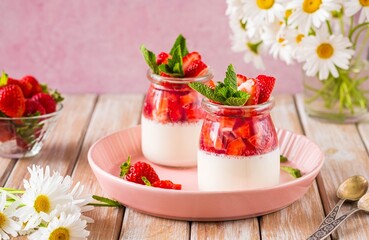Dessert, creamy panna cotta with fresh strawberries in glass jars on a light wooden background. Dessert recipes without baking.