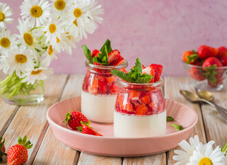 Dessert, creamy panna cotta with fresh strawberries in glass jars on a light wooden background. Dessert recipes without baking.