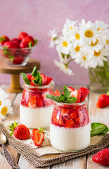 Dessert, creamy panna cotta with fresh strawberries in glass jars on a light wooden background. Dessert recipes without baking.