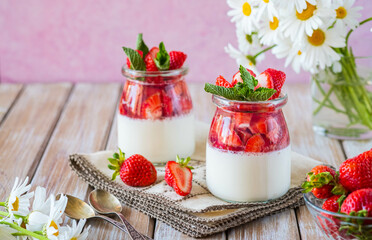 Dessert, creamy panna cotta with fresh strawberries in glass jars on a light wooden background....