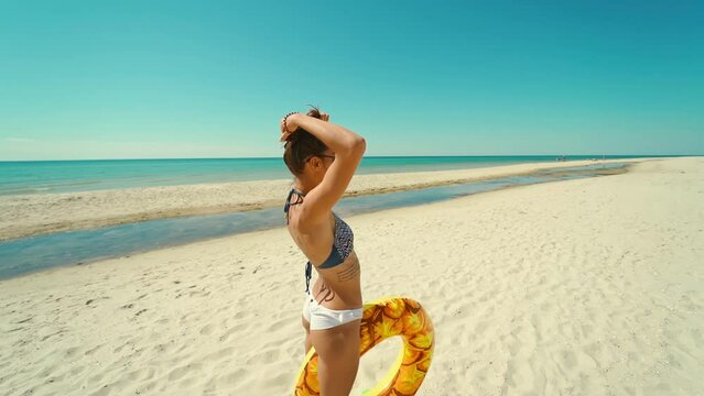 Cheerful happy young attractive woman runs on empty sunny sandy beach holding yellow inflatable pineapple floating ring at summer sea travel. 20s. 1080p Slow Motion.