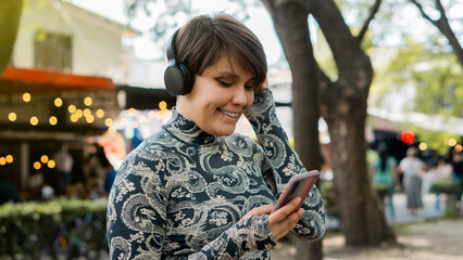 Woman walking and smiling listening to music with her cell phone and headphones in the park.