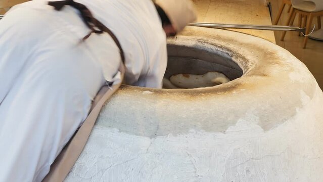 a Georgian male baker stuck raw dough on the inner wall of a stone tonir while baking ojakhuri