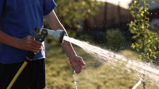 child plays with water hose sprinkler in the garden. Sunny Summer Day children playing in the backyard. In Slow Motion