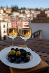 Glass bowl with black andalusian olives served with sherry wine on outdoor terrace with view on old part of Granada, Andalusia, Spain