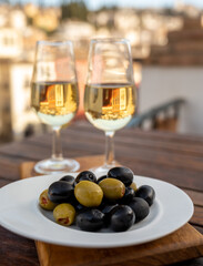 Glass bowl with black andalusian olives served with sherry wine on outdoor terrace with view on old part of Granada, Andalusia, Spain