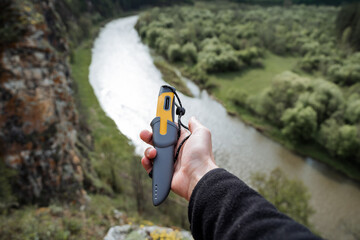 A beautiful knife lies in the palm of a man's hand, a tourist holds a hiking knife in a case, a gray plastic sheath, a trip alone, summer holidays in nature.