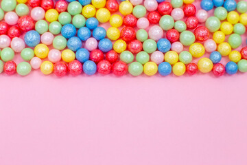 Multi-colored round glossy balls of sugar confectionery topping lie at the down on a pink background.