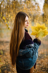 A long-haired caucasian woman with big lips with a bouquet of yellow maple leaves poses in an autumn park. Medium shot.