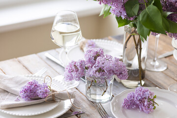 Beautiful table decor for a wedding dinner with a spring blooming lilac flowers. Celebration of a special event. Fancy white plates, wineglasses. Countryside style