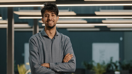 Portrait dreaming handsome millennial indian arabian young man hispanic guy businessman male worker analyst manager leader turn head looking at camera posing stand in modern office with crossed arms