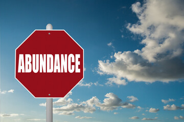 Red stop sign with the word Abundance on a blue sky background.
