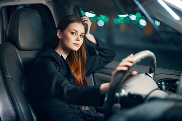 a happy, relaxed woman enjoys a night drive while sitting in a car and holding her hand near her head in a relaxed pose