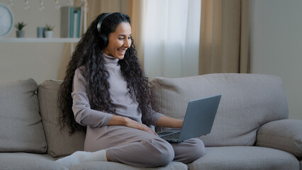 Happy smiling woman young pretty arabian girl freelancer at home apartment wear headphones talk video call online use computer internet social app greeting friend wave hand enjoy virtual conversation