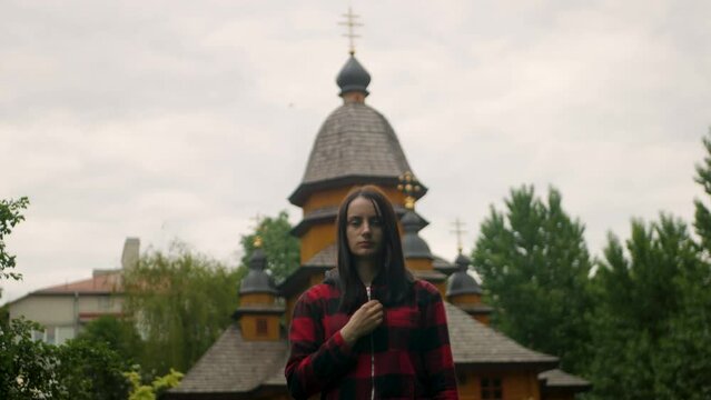 Beautiful white female showing Christian sign of the cross in front of a church. Long-haired religious female symbolizes her faith in God with cross gesture. Concept of believing in God and devotion
