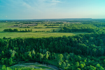Aerial shot of green fields, forests and a creek bending in the foreground